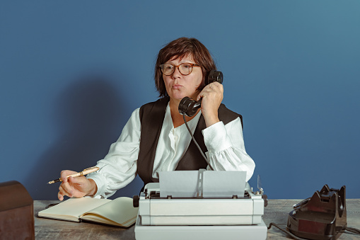 Secretary woman from the past at work. Table with telephone and typewriter. Vintage.