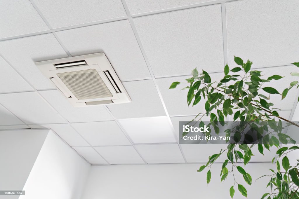 Low angle of assette Air Conditioner on ceiling in modern light office or apartment with green ficus plant leaves. Indoor air quality Cassette air conditioner on ceiling in modern light office or apartment with green ficus plant leaves. Indoor air quality and clean filters concept Quality Control Stock Photo
