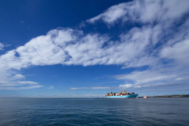 Panorama of the Adriatic sea in the port of Koper, Slovenia, with a container ship, full of containers and cargo, ready to be escorted to leave the port to exports goods and merchandises. Picture of a container ship on a panorama of the port of Koper, Slovenia, leaving the port to export goods. koper slovenia stock pictures, royalty-free photos & images