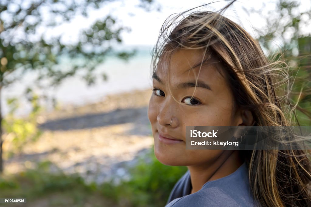 Gorgeous Chinese woman enjoys the wind blowing through her hair by the ocean in Maine Natural beauty exudes from this young adult enjoying a sunny day by the ocean in New England. One Woman Only Stock Photo