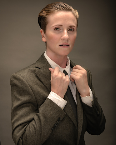 A non-binary citizen of Los Angeles poses in studio wearing a jacket, shirt and tie.