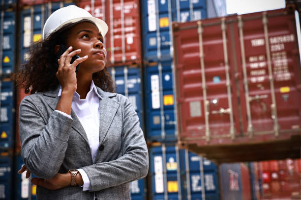 retrato de mujer bronceada en la fábrica en el patio de contenedores, mujer yong con casco de seguridad de pie discusión comercial en el año del contenedor, negocio logístico y concepto de cadena de suministro - industrial ship dock worker engineer harbor fotografías e imágenes de stock