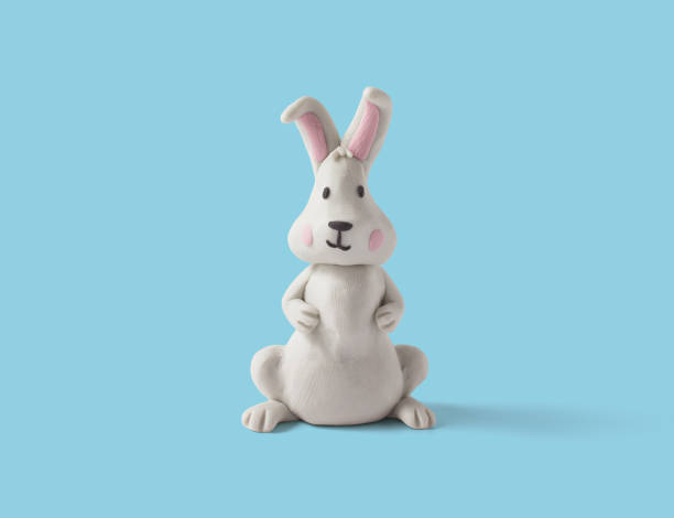 istock Cute sitting rabbit made of white plasticine on a blue background. Handmade easter rabbit in clay. 3d artwork 1410387408
