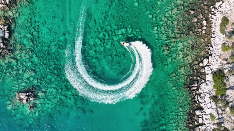 Amazing aerial view of man driving a personal watercraft in the ocean creating a straight down circular pattern, nature background, Water color and beautiful bright Clear turquoise Adventure day on tropical beach Spinning speed boat, summer background