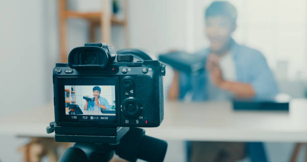 gros plan d’un jeune blogueur ouvrant une boîte à colis et enregistrant une vidéo de déballage avec une caméra assise à un bureau dans le salon à la maison. - youtube home video camera internet ipad photos et images de collection