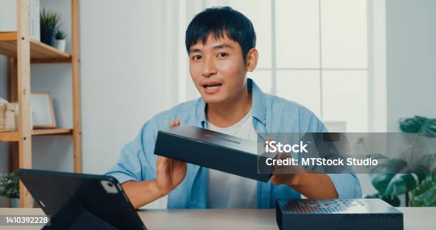 Young Man Blogger Opening Parcel Box And Recording Unboxing Video With Camera Sitting At Work Desk In Living Room At Home Stock Photo - Download Image Now
