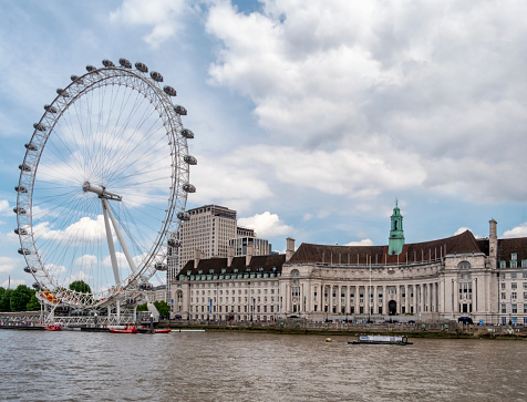 LONDON, JULY 2017 - View of Westminster Parliament, Big Ben and London Eye with Thames and tourist ship in foreground on a sunny summer afternoon