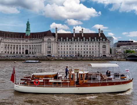 The Wairakei II motor yacht moving along the River Thames in front of the former County Hall building with two passengers aboard. The Wairakei II was built in 1932 and is one of the “Dunkirk Little Ships”, reputed to have saved the lives of around 150 soldiers from the beaches of Dunkirk in the spring of 1940.