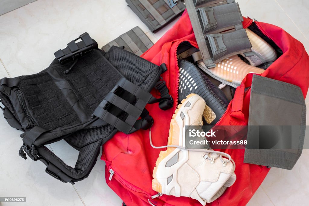 tactical equipment in mess tactical boots, magazine holders and bulletproof vest in red travel bag Army Stock Photo