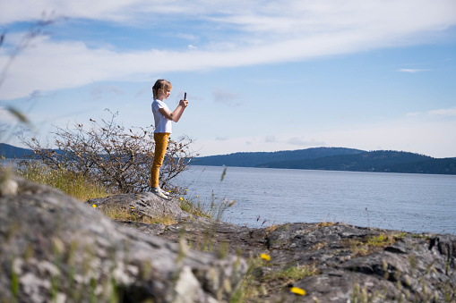 Exploring nature and the outdoors. Young girl with a mobile phone taking pictures while on vacation