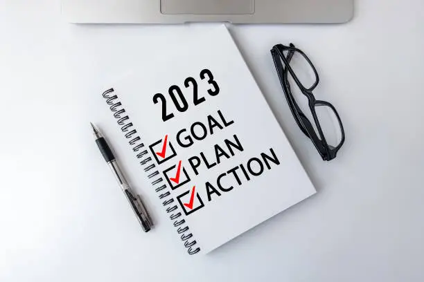 Photo of 2023 Goal, Plan, Action checklist text on note pad with laptop, glasses and pen.