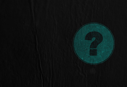 A faded question mark symbol over a grey colored  grunge circular backdrop over black wrinkled background. There is ample copy space and no people.