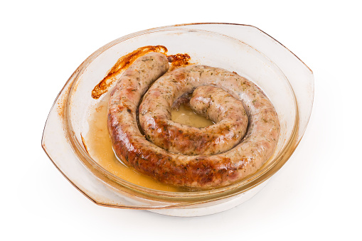 Coiled baked pork sausage with herbs in natural casing in the glass baking dish on a white background