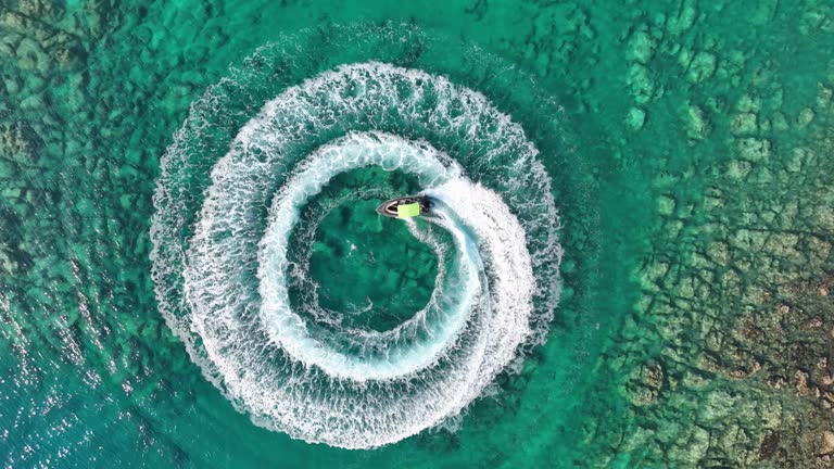 4K zoom out amazing aerial view of man driving a personal watercraft in the ocean creating a straight down circular pattern,Amazing summer background, Water color and beautiful bright Clear turquoise Adventure day on tropical beach, Spinning speed boat