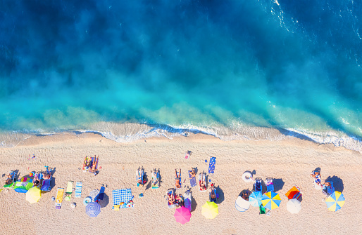 Aerial view on the beach, people and umbrellas. Vacation and adventure. Beach and blue water. Top view from drone at beach and azure sea. View on the coast from drone.