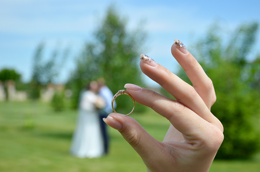 a gold engagement ring with a stone in a womans hand in the background a blurred silhouette of a couple in love kissing during a wedding photo shoot