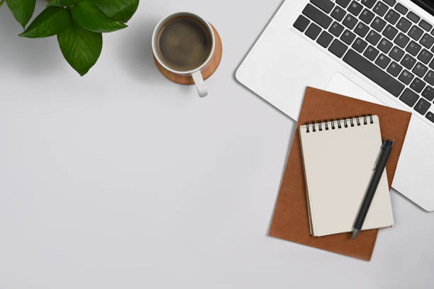 istock Simple workplace with laptop, notepad, coffee cup and houseplant on white table. 1410419339