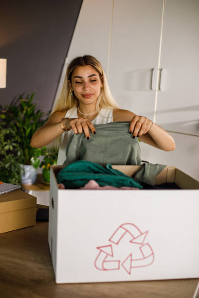 молодая женщина складывает свою старую зеленую куртку, чтобы упаковать в коробку для благотворительности - life jacket despair business life стоковые фото и изображения