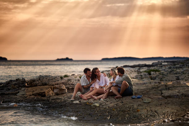 istock Young happy couples talking on rocky beach at sunset. 1410422547
