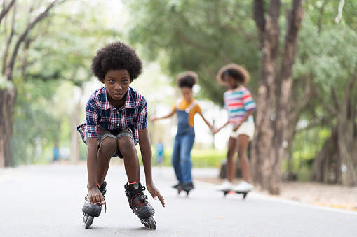 Happy young boy playing on roller blades in the park, African American young boy riding roller blades in the garden, Kid practicing roller blades.
