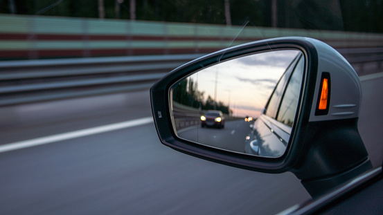 Close-up of side-view mirror of the car on the move at the highway in the evening