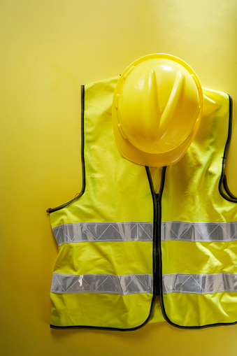 hardhat and reflective vest against yellow color background