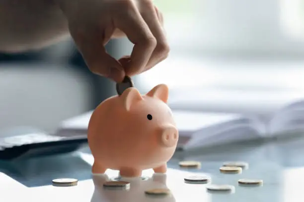 Photo of Close up male hand putting coins inside small piggybank.