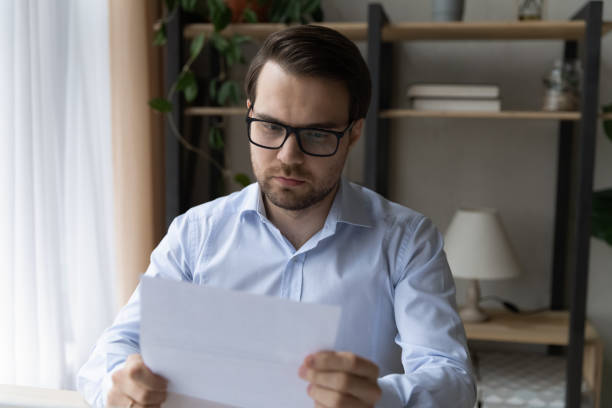 istock Concentrated young male manager in glasses reading paper document. 1410434752