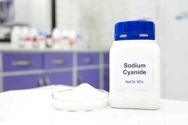 Selective focus of a bottle of Sodium Cyanide pure chemical compound used for illegal cyanide fishing. White laboratory background.