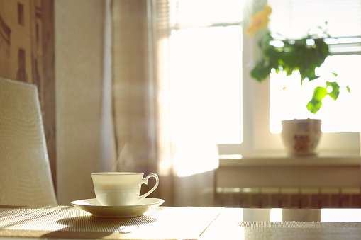 a cup of hot steaming coffee on a sunny morning on the kitchen table