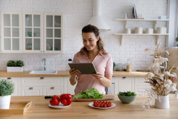 istock Joyful young woman using digital computer tablet, preparing food at home. 1410442283