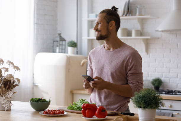 istock Happy young man using cellphone, preparing food. 1410442285
