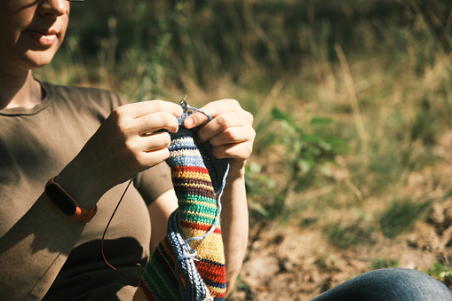 Mature woman is sitting under the tree  in nature park and knitting