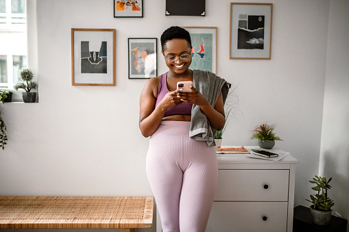Young woman using smartphone, preparing for home yoga workout class.