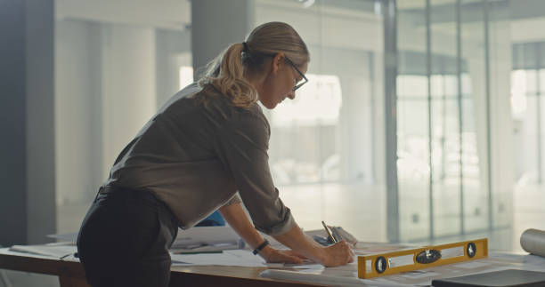 istock Architect drafting blueprint plans for a building and construction project. Dedicated female industrial designer and engineer developing a layout and adjusting measurements for property development 1410445014