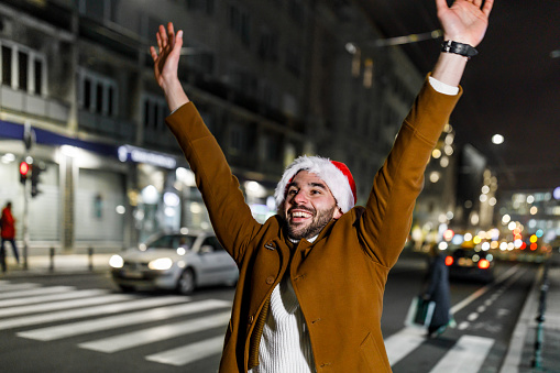 A Man in Warm Clothingis Raising his Hand and Trying to Catch a Ride in the City During a Night.