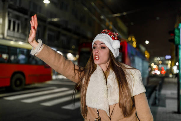 una giovane donna con il cappello di babbo natale è in piedi per strada e saluta per prendere un taxi. - christmas fashion model human arm beautiful foto e immagini stock