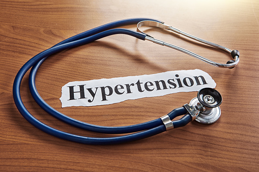 Hypertension, says newspaper headline surrounded by a stethoscope on a doctor's wooden desk.