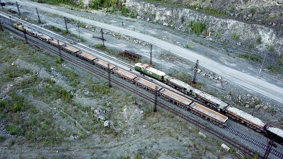 Diesel locomotive is pushing dump-car filled with rubble stone in the background of a quarry for limestone mining.