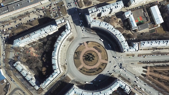 Top view of roundabout in city center. Roundabout with busy traffic of cars, surrounded by houses in city center on sunny day.