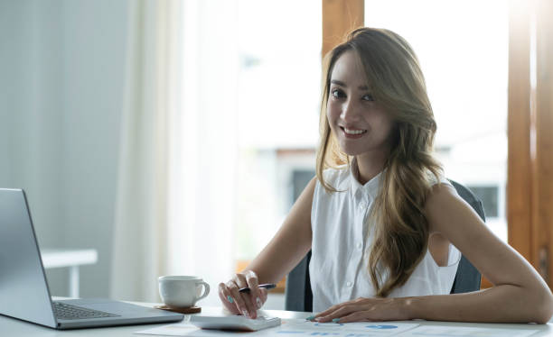 istock Charming Asian woman working at the office using a laptop Looking at the camera. 1410448987