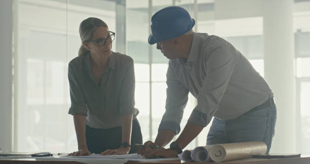 istock Architect and contractor discussing building plans for a construction project. Civil engineer and builder collaborating to design, develop and assess a layout for commercial property development 1410449219