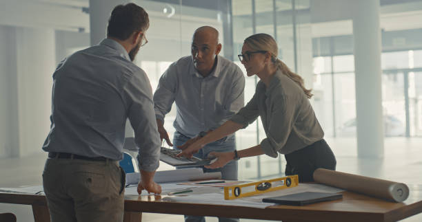 istock Group of architects using blueprints and paperwork to discuss building plans. Diverse engineer colleagues and contractors thinking, talking and planning structure development to design home or office 1410450381