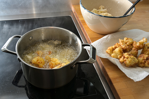 Deep fried cauliflower in process, frying in hot cooking oil in a pot, drying on a paper towel and raw in a bowl, preparation of a vegetarian snack, copy space, selected focus, narrow depth of field