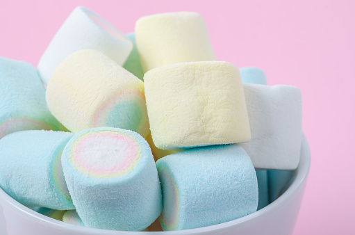 Mini colorful marshmallows in cup on pink background.