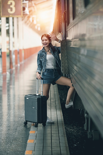 Young asian female traveler in blue jeans and luggage stepping on the train to travel alone.