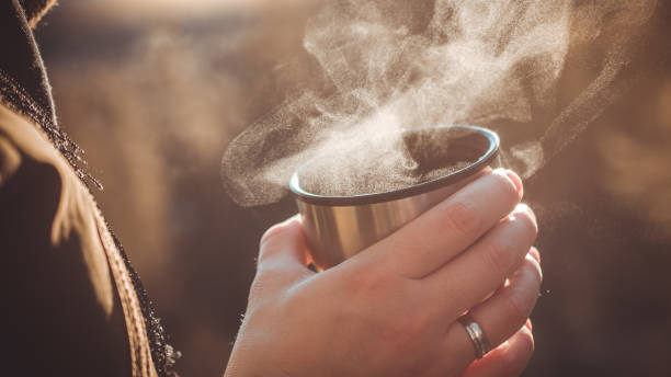 Person holds hot tea in a thermos cup (drops of steam freeze in the cold). stock photo