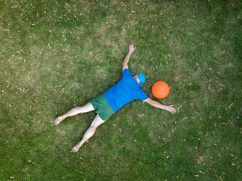 exhausted senior man lying down on a grass and resting after heavy slam ball workout, view from above