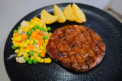 Rounded shape beef rib eye steak with potato wedges and vegetables