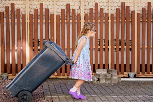 Little preschool girl with glasses taking garbage can. child learning waste sorting. Environment concept